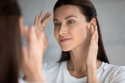 Close up beautiful woman looking in mirror in bathroom, touching face, pretty young female checking makeup, satisfied by healthy perfect skin, natural beauty concept, face care and treatment