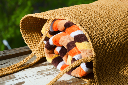 Beach bag in raffia with colorful towel. Women's bag on the background of green trees. Hobby, needlework.