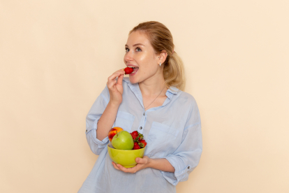 front-view-young-beautiful-female-shirt-holding-plate-with-fruits-eating-strawberry-cream-wall-fruit-ripe-model-woman-pose